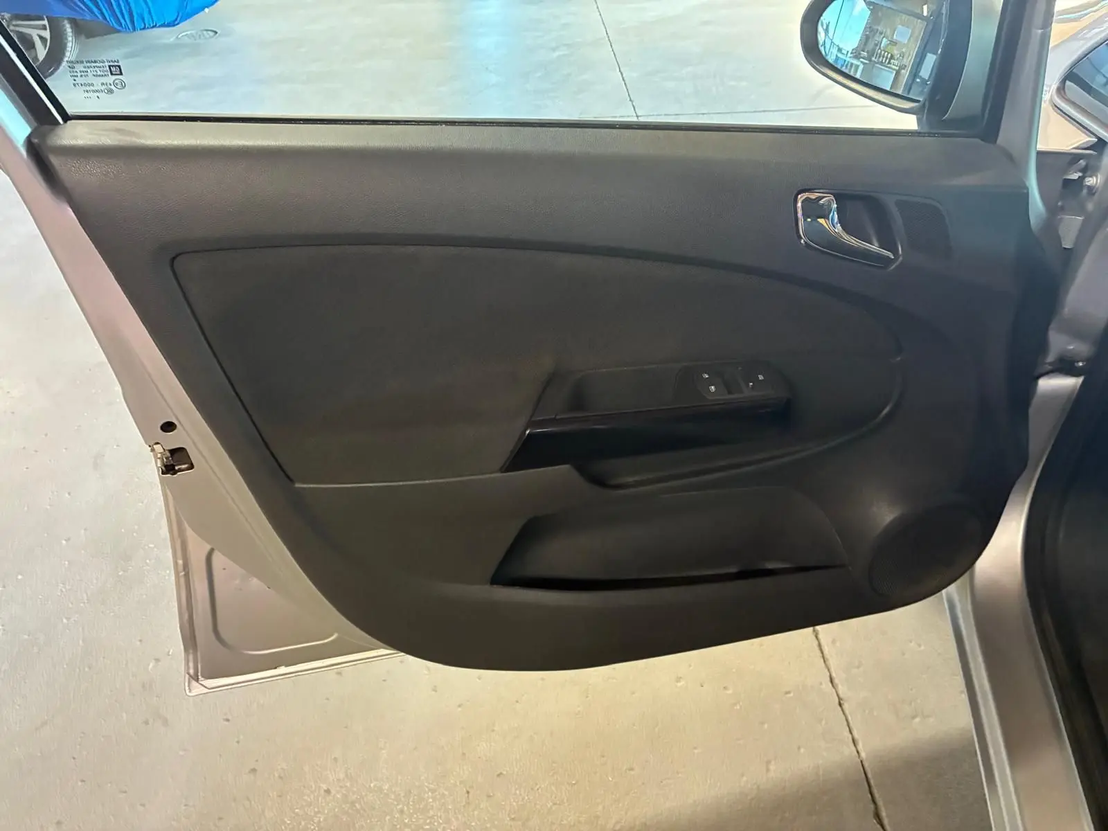 Vue intérieure de la porte avant gauche gris clair de l’Opel Corsa 1.2i 85 Edition avec garniture noire et commandes de vitres.