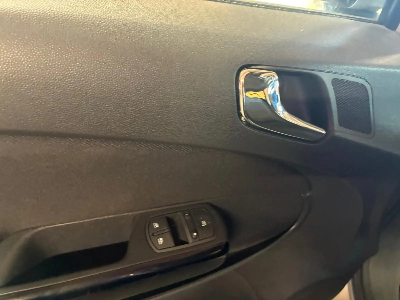 Gros plan sur la poignée intérieure et les commandes de lève-vitres côté gauche d’une Opel Corsa gris clair 2012.