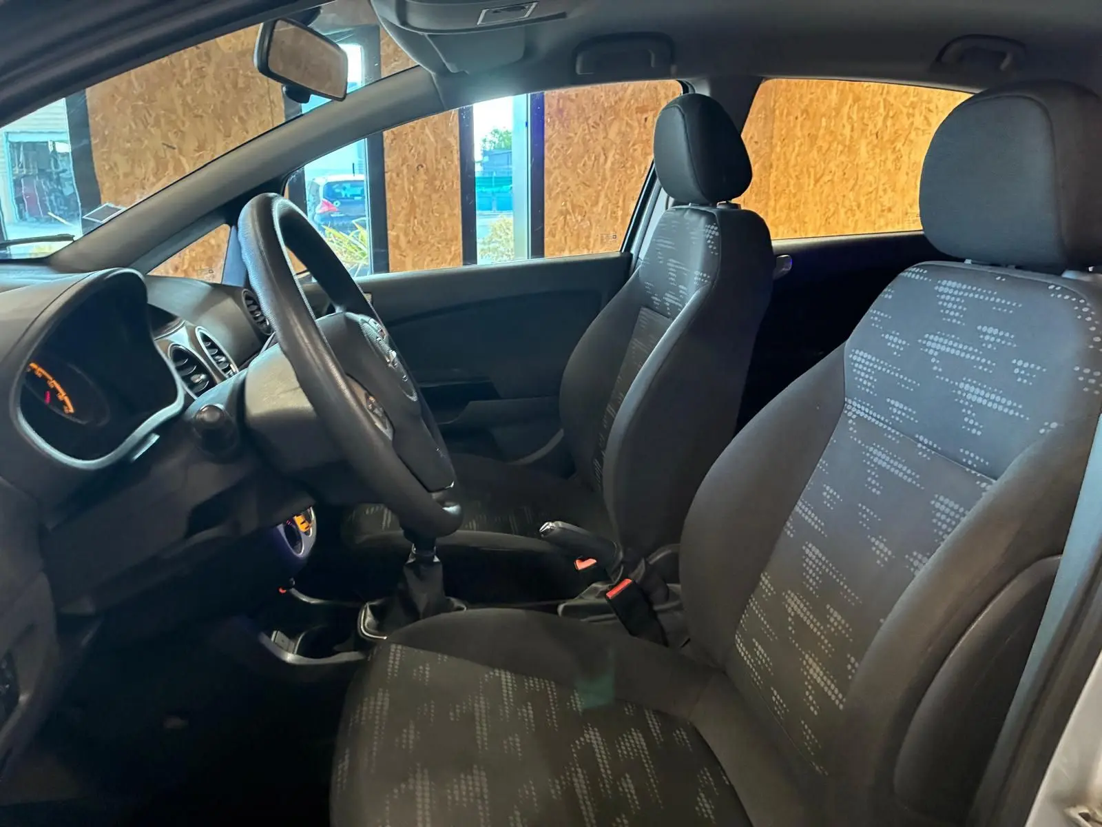 Vue intérieure côté conducteur de l’Opel Corsa gris clair 2012, sièges tissu noir avec motifs et volant multifonction.