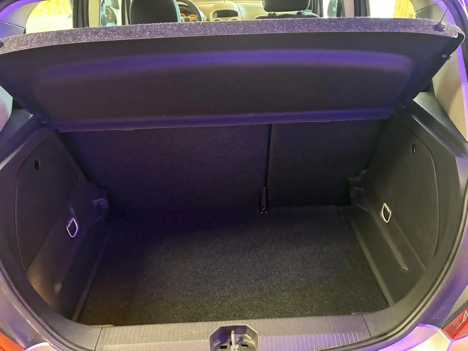 Coffre ouvert de l’Opel Corsa gris clair 5 portes, vue arrière montrant l’espace de rangement et la moquette noire.
