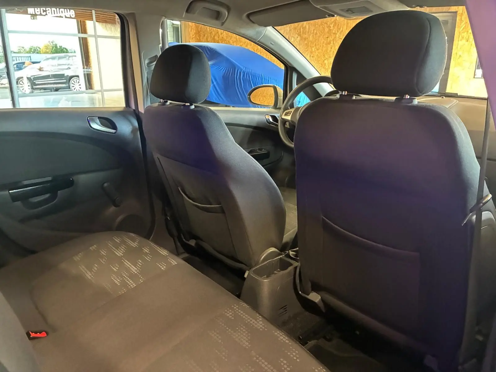 Vue intérieure arrière de l'Opel Corsa 2012 avec sièges en tissu noir et portes arrière visibles côté gauche.