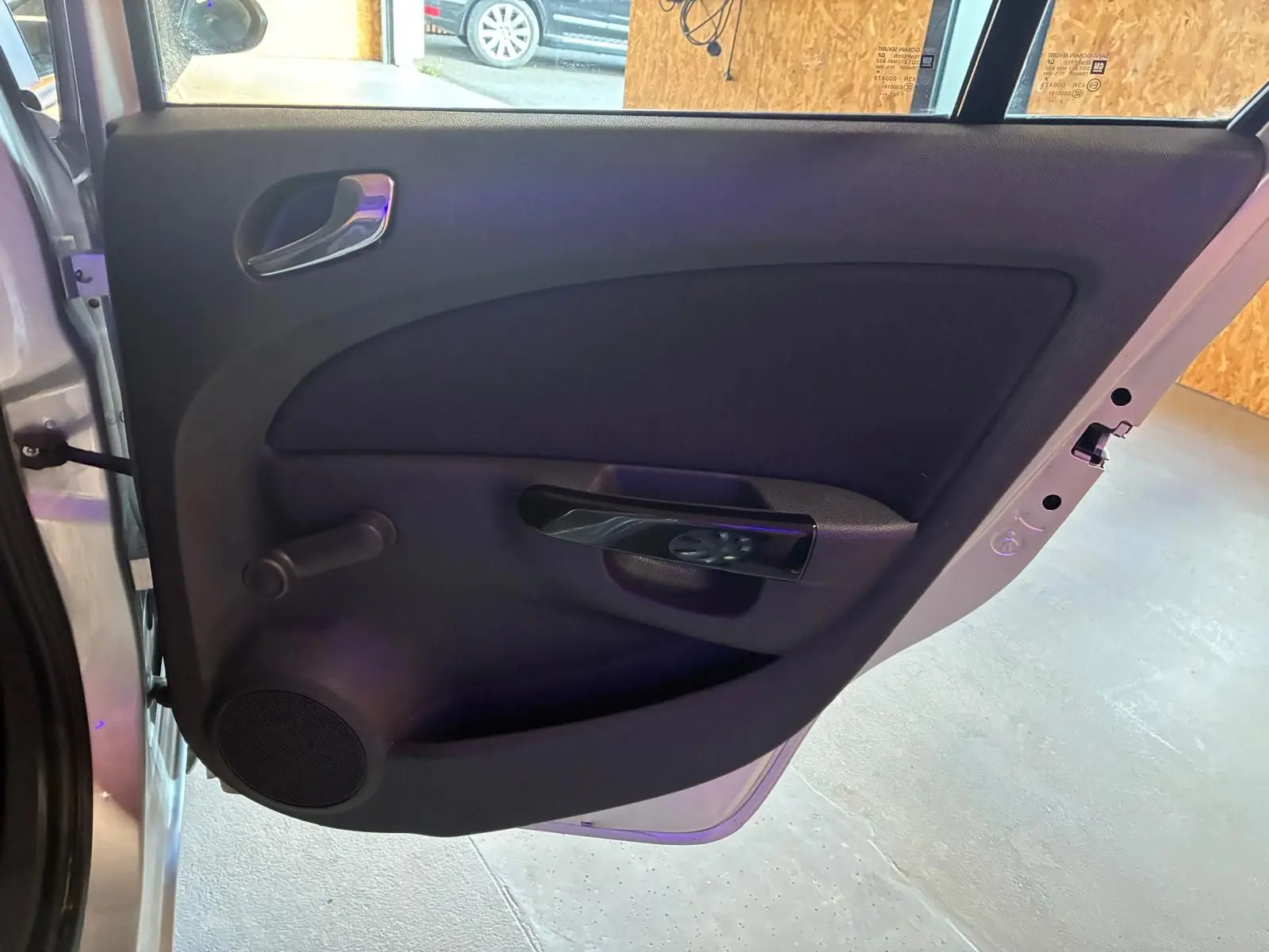 Vue rapprochée de la porte arrière gauche ouverte d’une Opel Corsa gris clair, avec poignée intérieure noire et manivelle de vitre.
