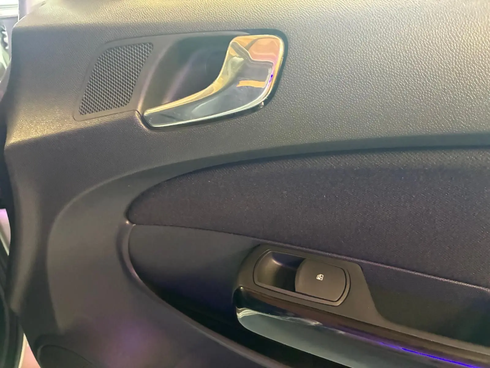 Gros plan sur la poignée intérieure chromée et le bouton de verrouillage sur la porte côté conducteur d’une Opel Corsa gris clair de 2012.