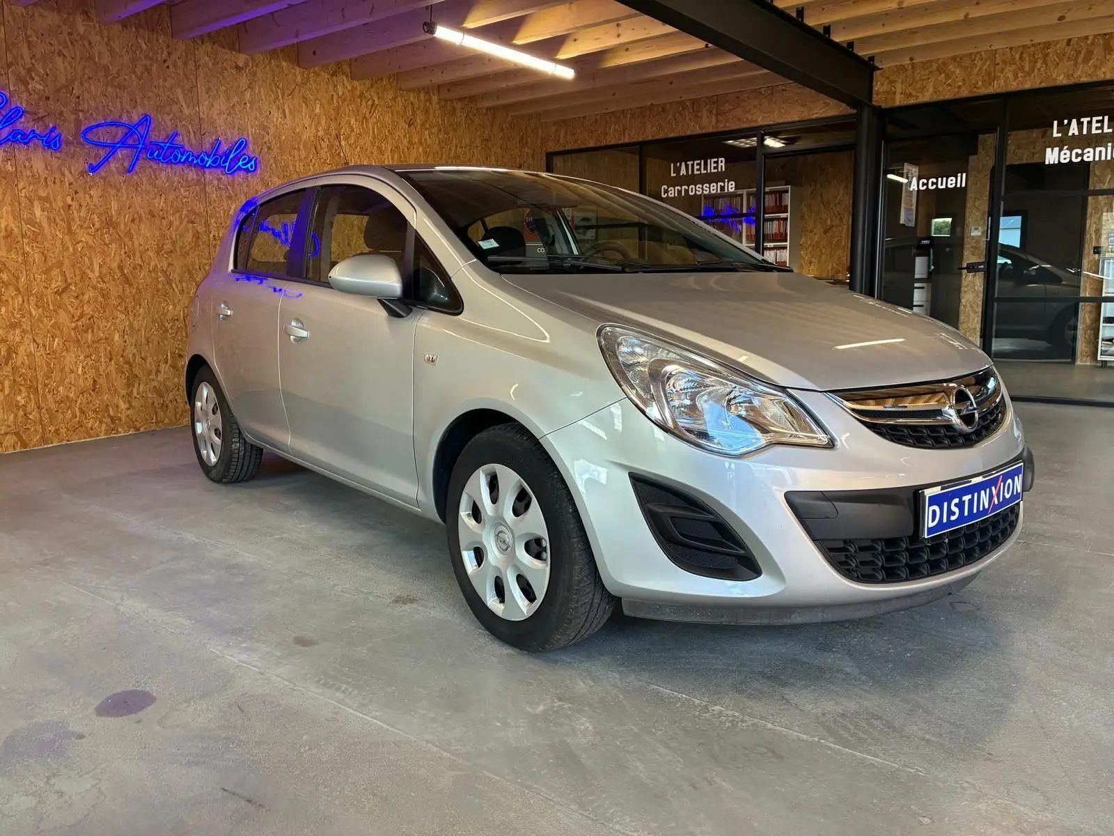Opel Corsa gris clair 2012 vue 3/4 avant droit, compacte cinq portes avec jantes acier et calandre chromée.