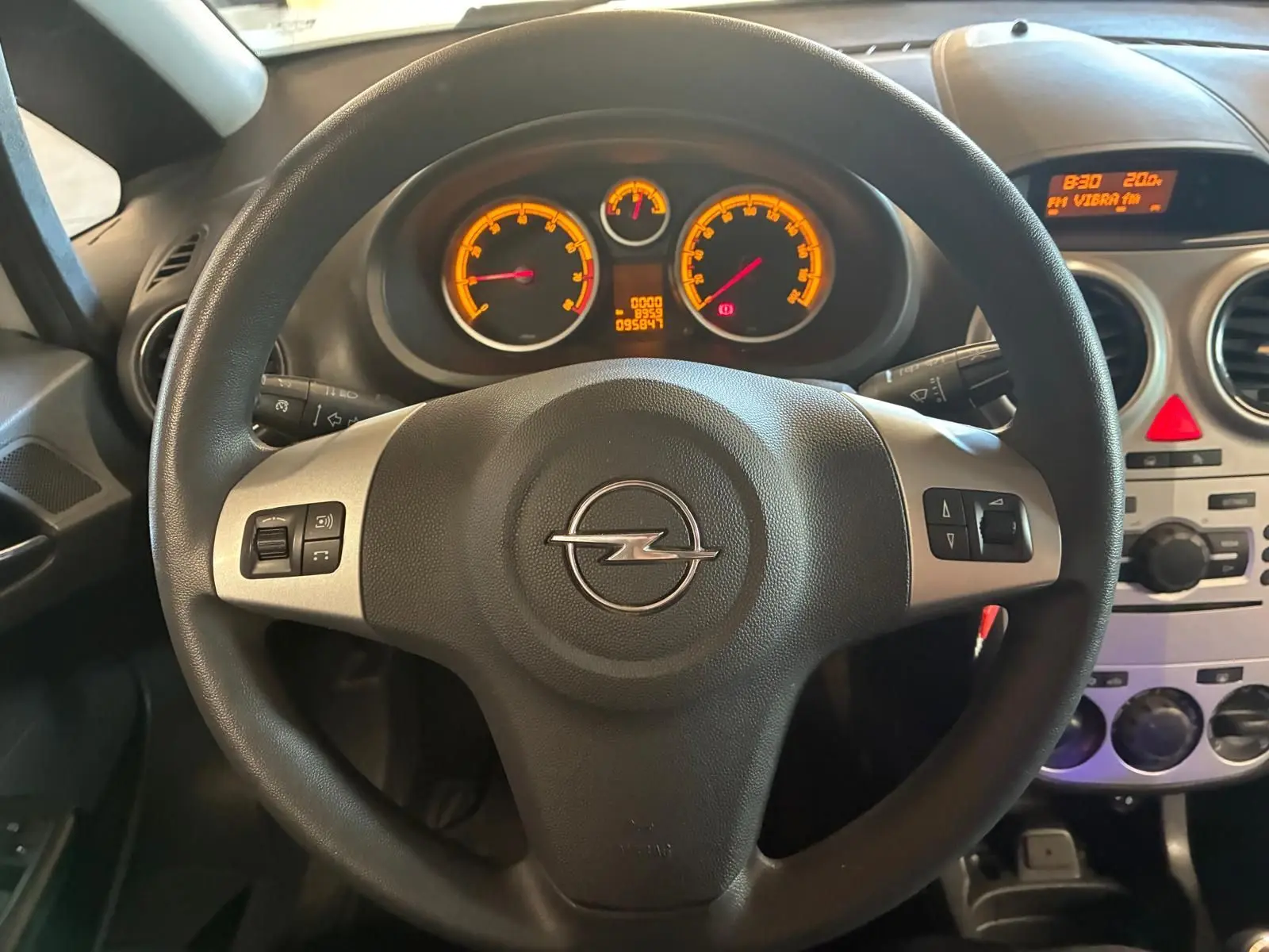 Vue intérieure centrée sur le volant noir d'une Opel Corsa 2012 avec tableau de bord et commandes visibles.