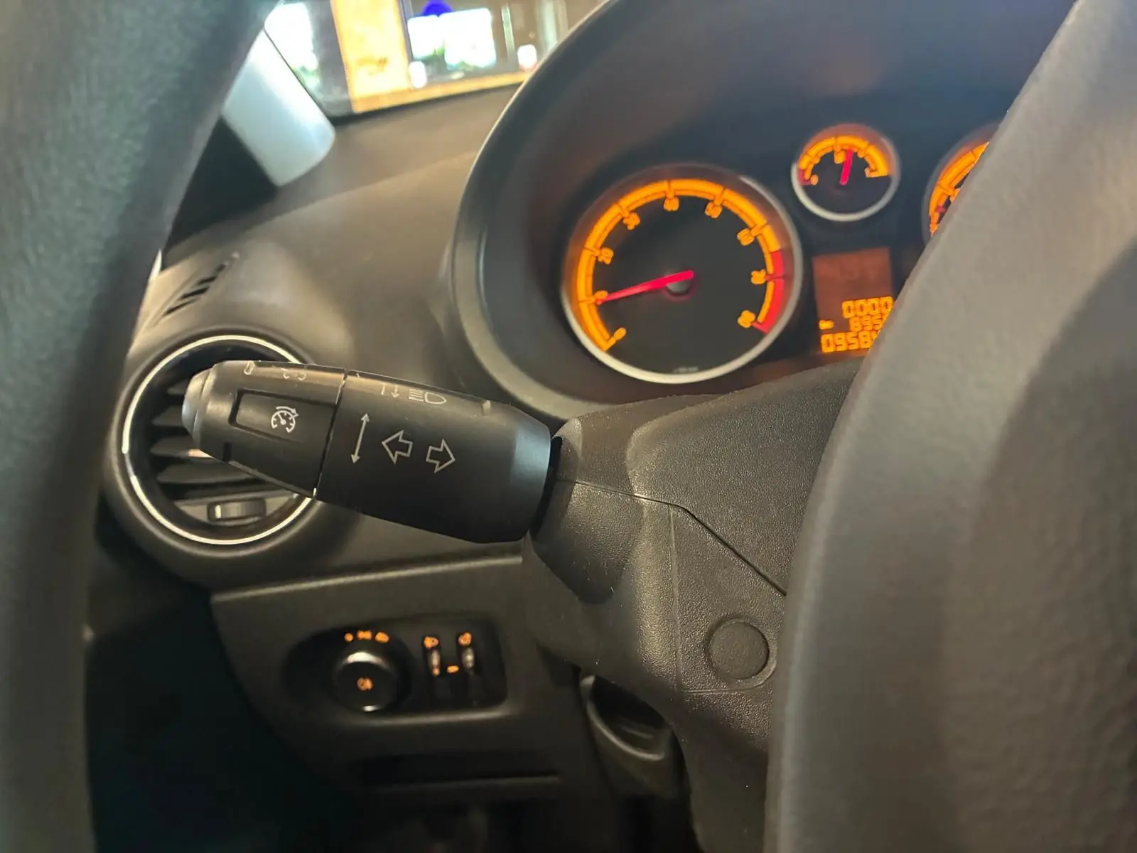 Gros plan sur le commodo gauche et le tableau de bord éclairé orange d'une Opel Corsa gris clair, vue depuis le siège conducteur.