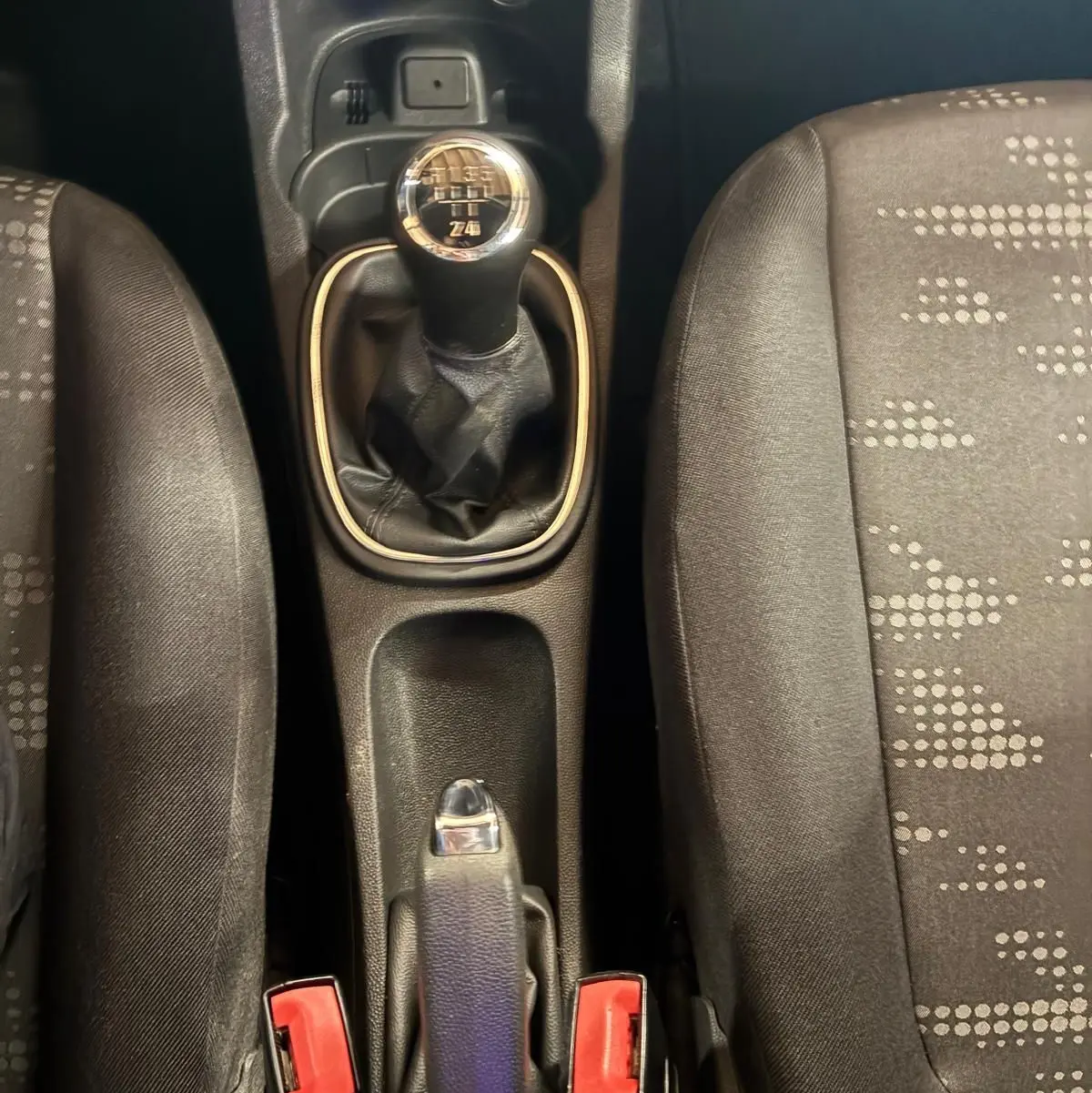Vue plongeante sur la console centrale d'une Opel Corsa gris clair, mettant en valeur le levier de vitesse manuel et les sièges en tissu noir.