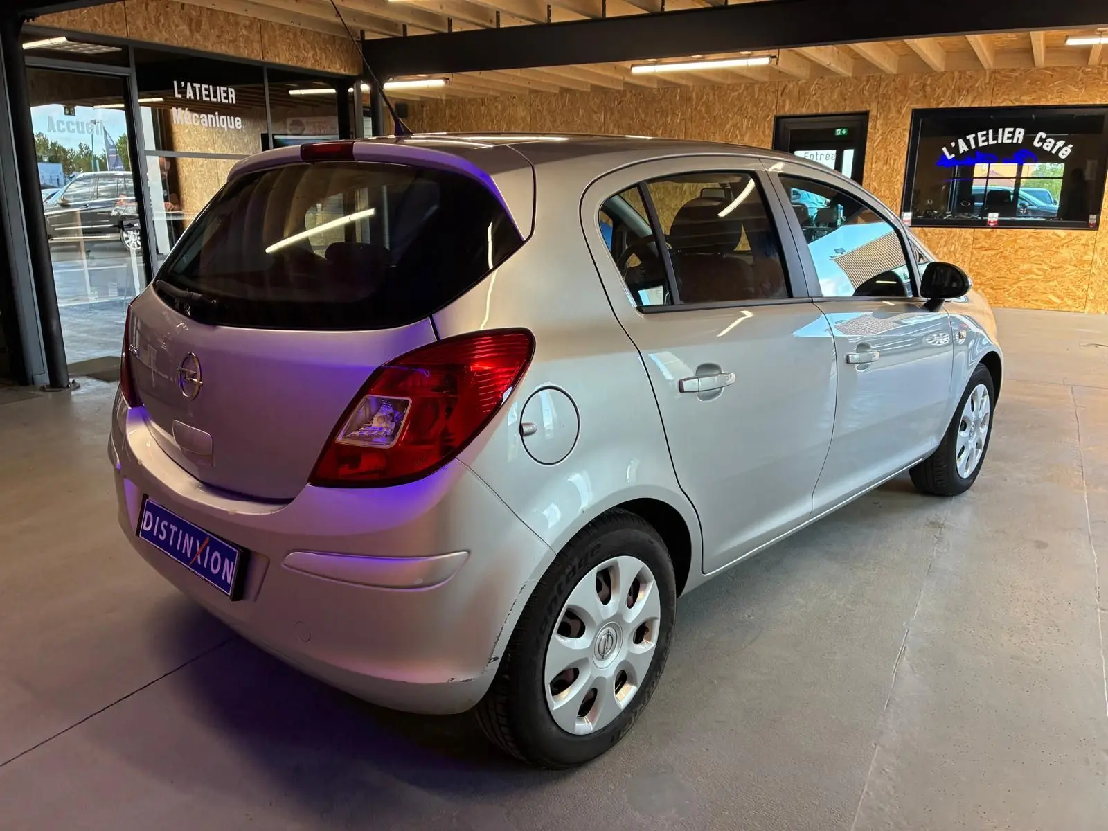 Opel Corsa gris clair vue 3/4 arrière droit dans un garage avec cinq portes et jantes acier.