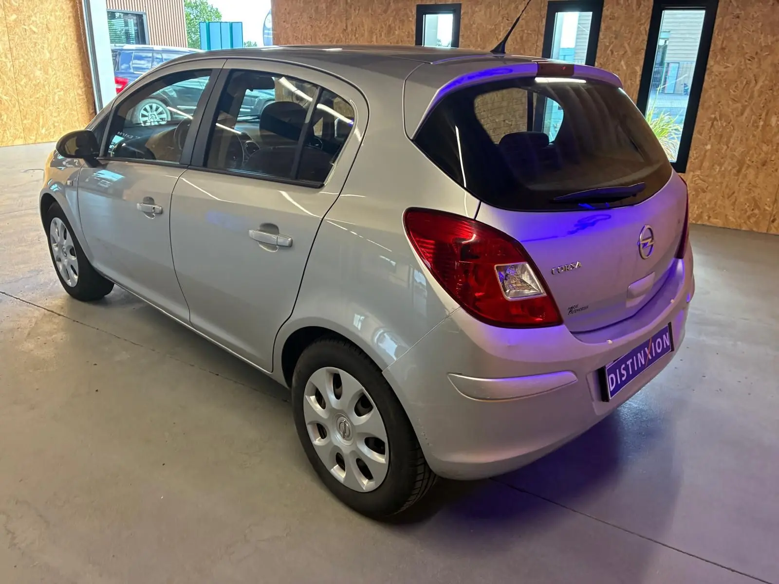 Opel Corsa gris clair vue 3/4 arrière droit, compacte 5 portes avec feux arrière rouges et jantes acier.