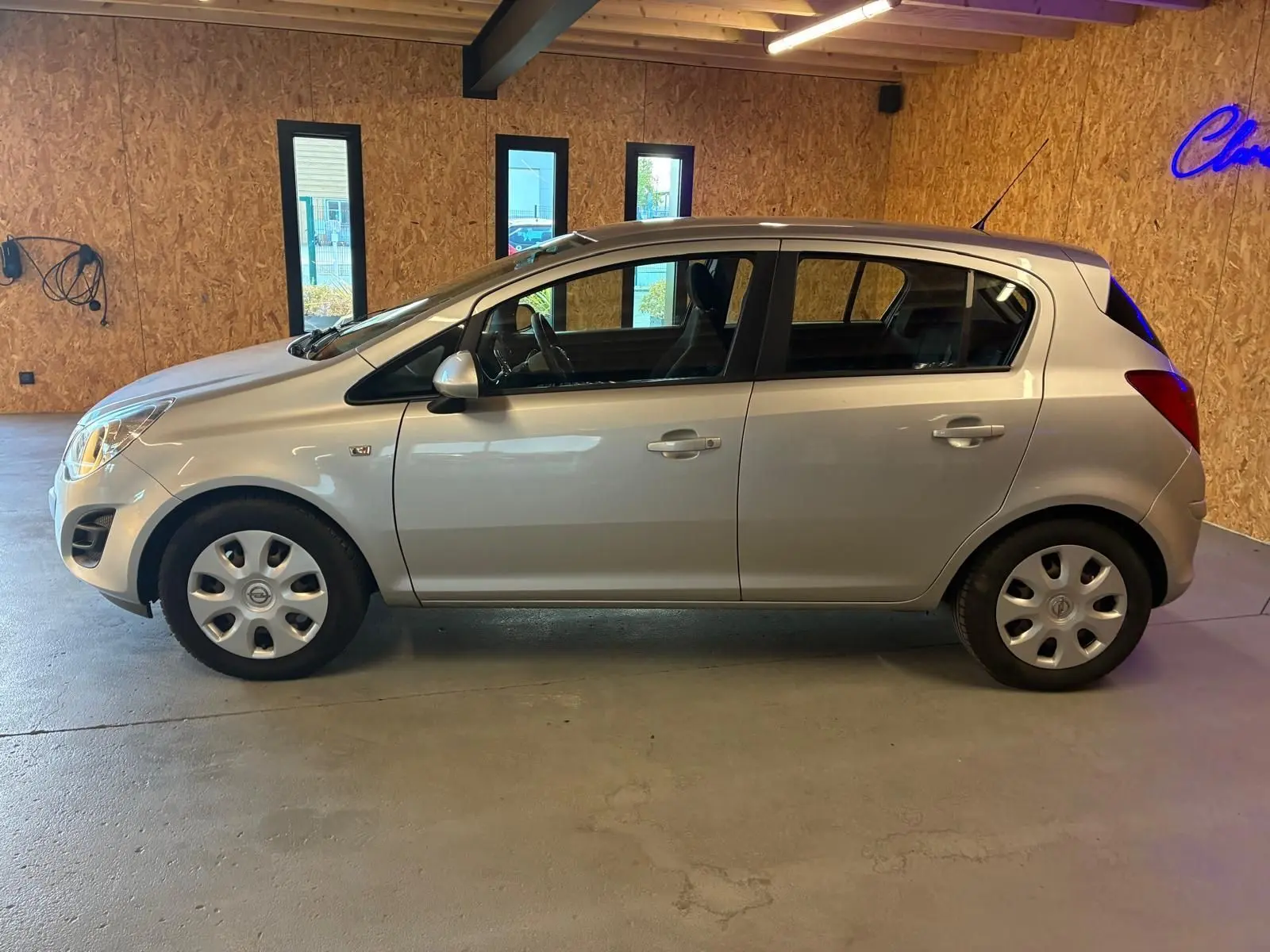 Vue latérale droite d'une Opel Corsa gris clair 5 portes de 2012, avec jantes acier et intérieur visible noir.