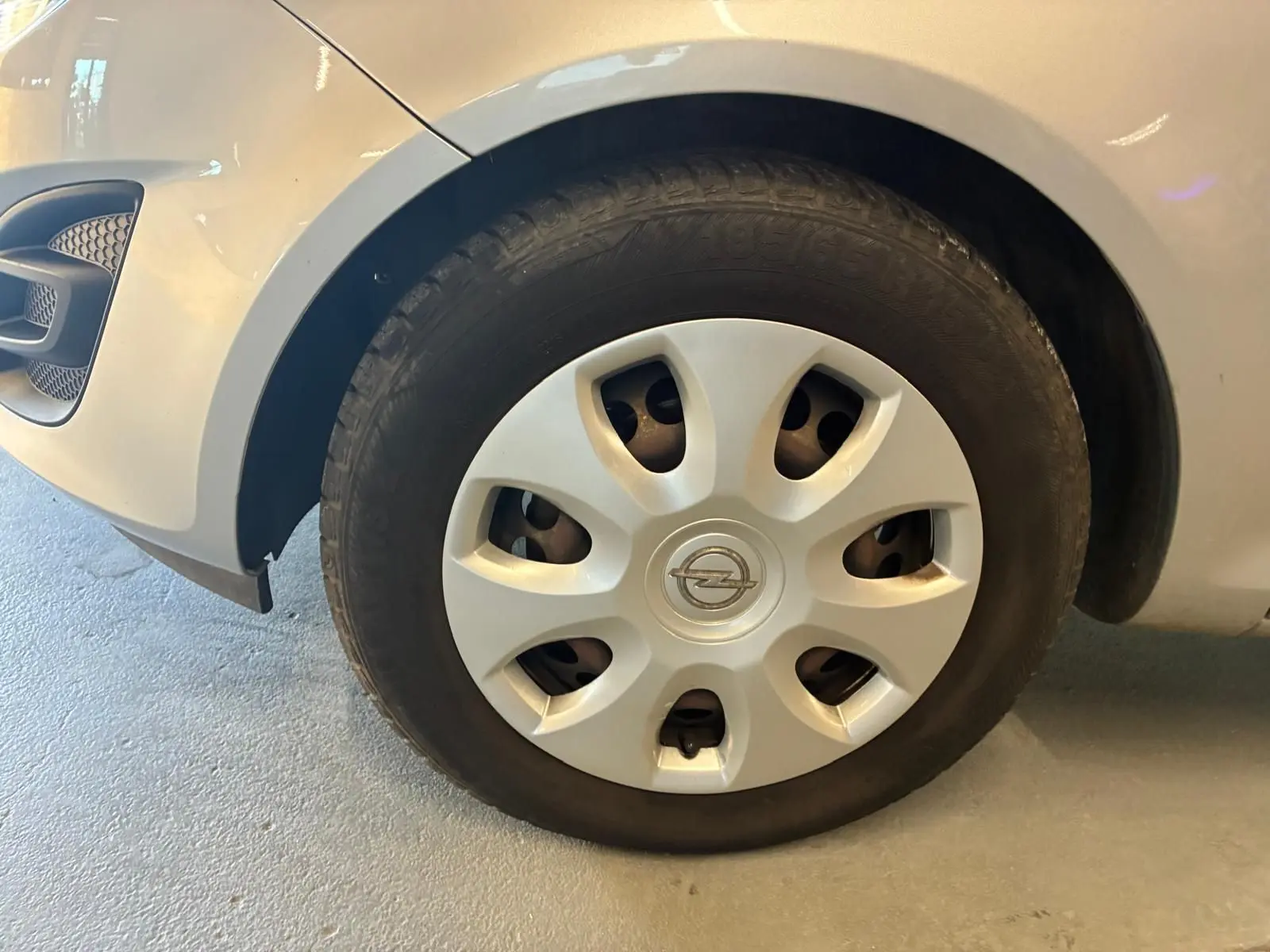 Gros plan sur la roue avant gauche grise claire d’une Opel Corsa 1.2i 85 Edition avec enjoliveur et logo Opel visible.