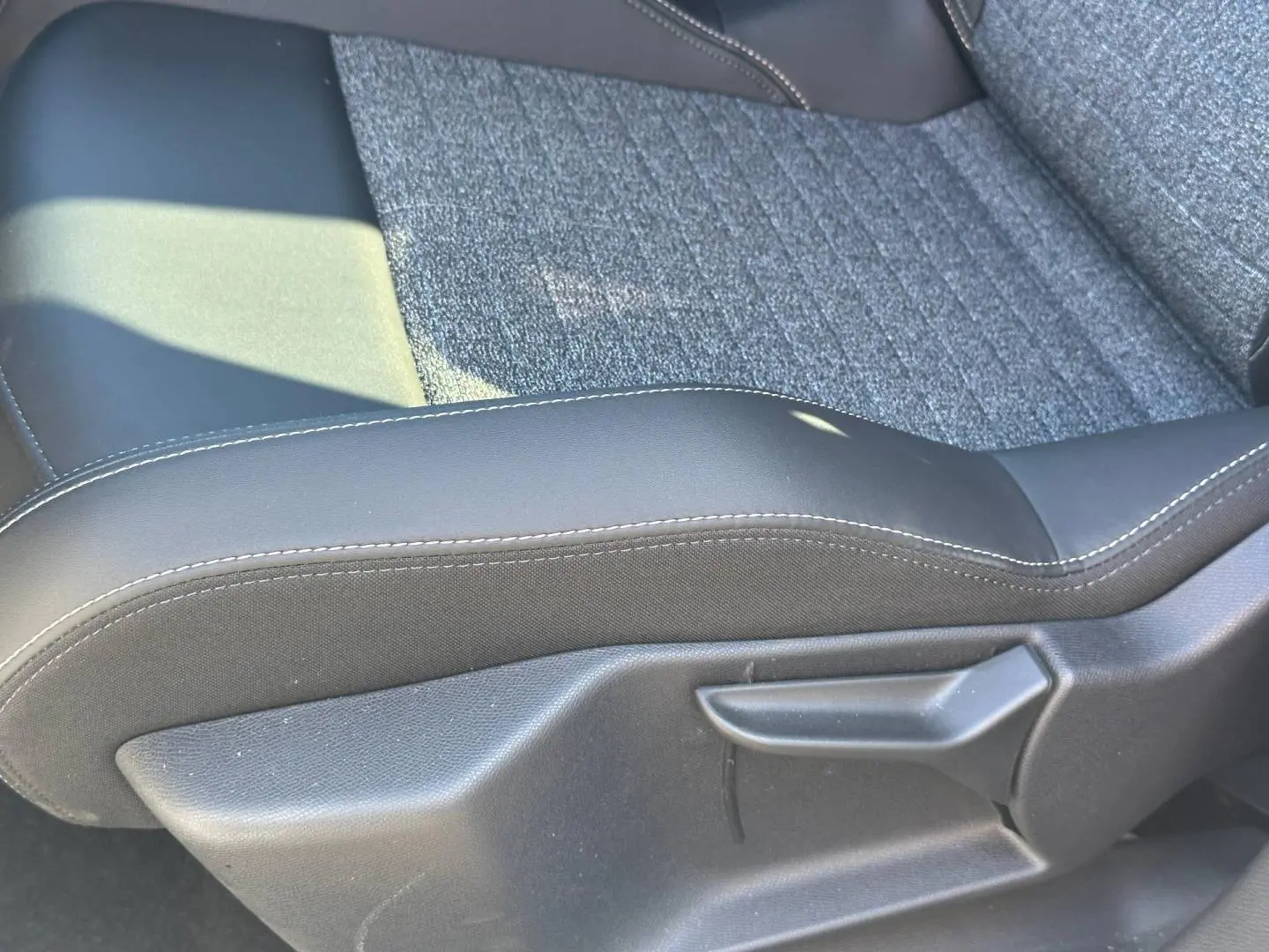 Gros plan sur l'assise en tissu gris et cuir noir avec surpiqûres blanches d'un siège avant Peugeot 5008 Hybrid 2025.