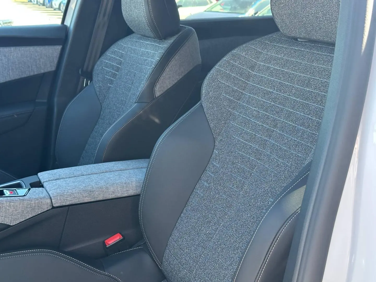Gros plan sur les sièges avant en tissu gris et cuir noir du Peugeot 5008 Hybrid blanc, avec accoudoir central.