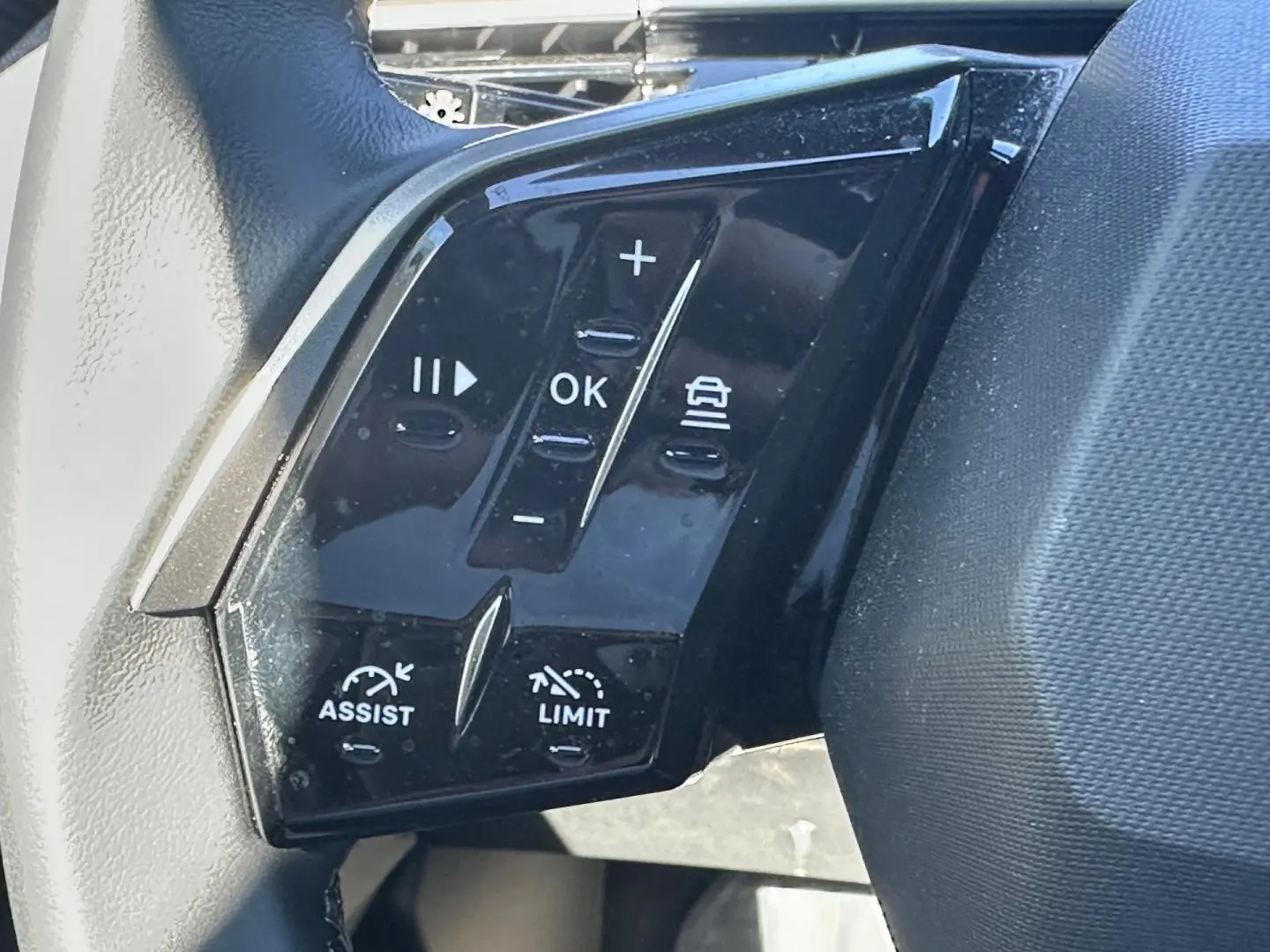 Gros plan sur les commandes multifonctions noires du volant cuir du Peugeot 5008 Hybrid blanc Okénite.