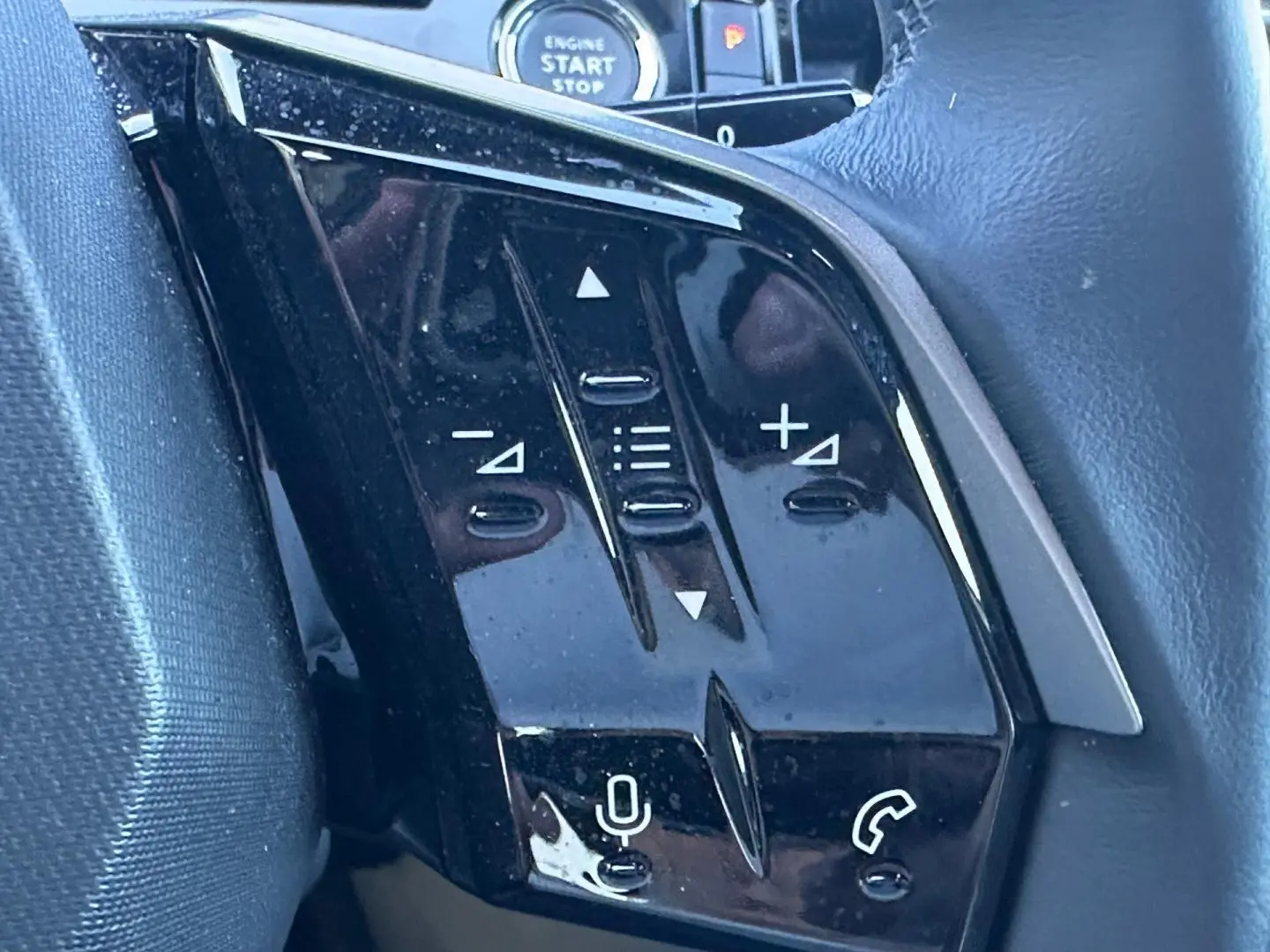 Gros plan sur les commandes noires du volant multifonction du Peugeot 5008 Hybrid blanc, avec bouton micro et téléphone.
