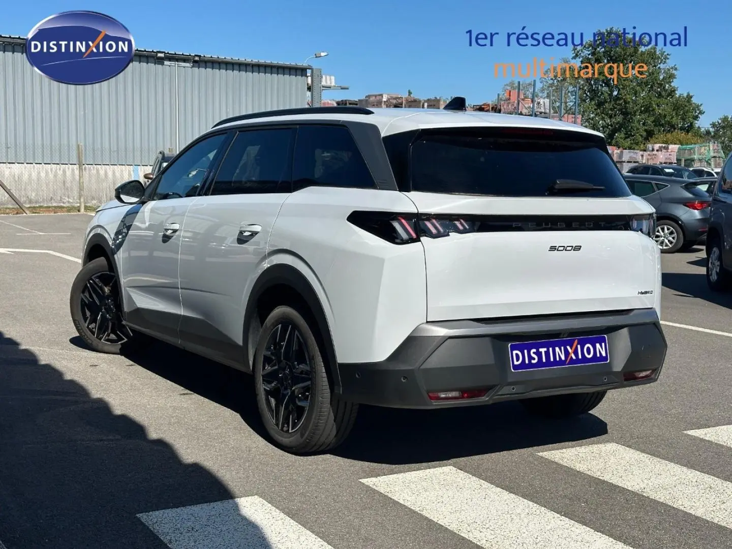 Vue 3/4 arrière droite d’un Peugeot 5008 Hybrid blanc Okénite avec vitres surteintées et jantes noires.