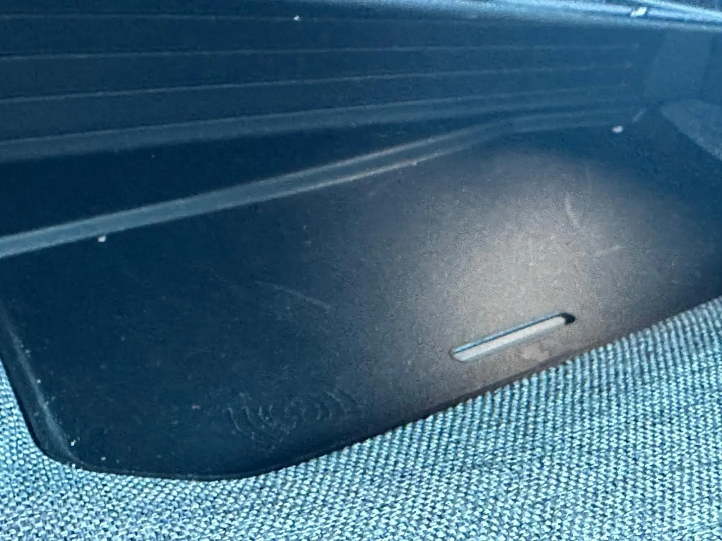 Gros plan sur le tapis de recharge sans fil noir dans l’habitacle du Peugeot 5008 Hybrid blanc Okénite.