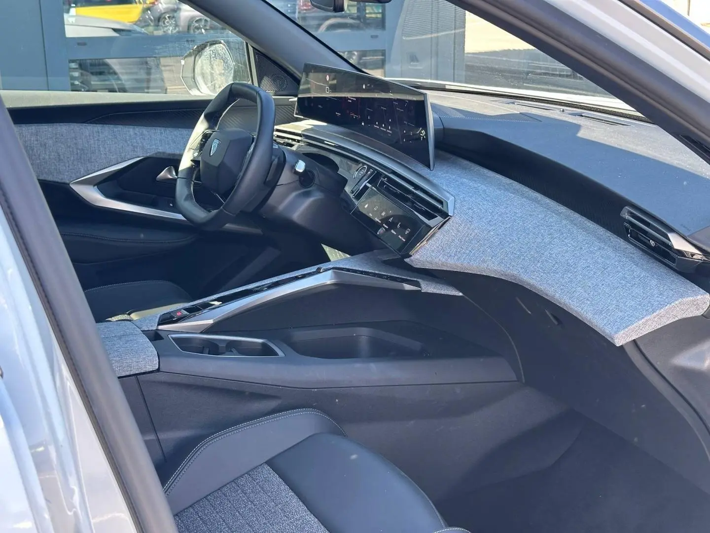 Vue intérieure côté conducteur du Peugeot 5008 Hybrid 2025, tableau de bord avec écran incurvé et tissu gris clair.