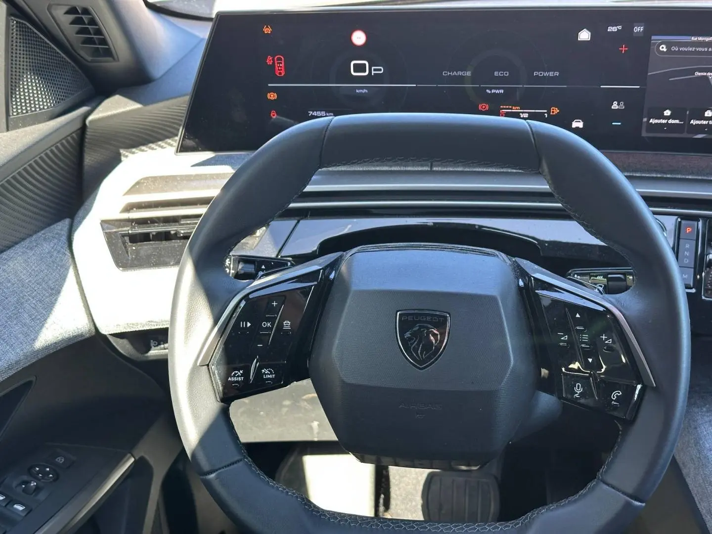 Vue rapprochée du volant cuir multifonction noir du Peugeot 5008 Hybrid 2025 avec tableau de bord numérique en arrière-plan.