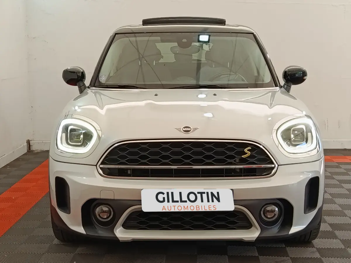 Vue avant d'une MINI Countryman Cooper SE blanche avec phares LED allumés et calandre noire à motif nid d'abeille.