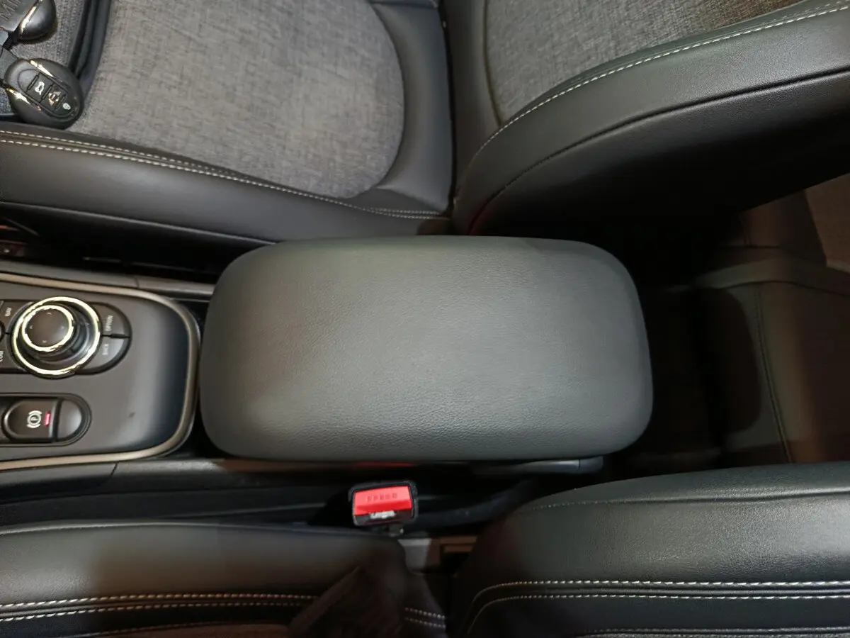 Gros plan sur l'accoudoir central noir et la console avec molette de la MINI Countryman hybride blanche.