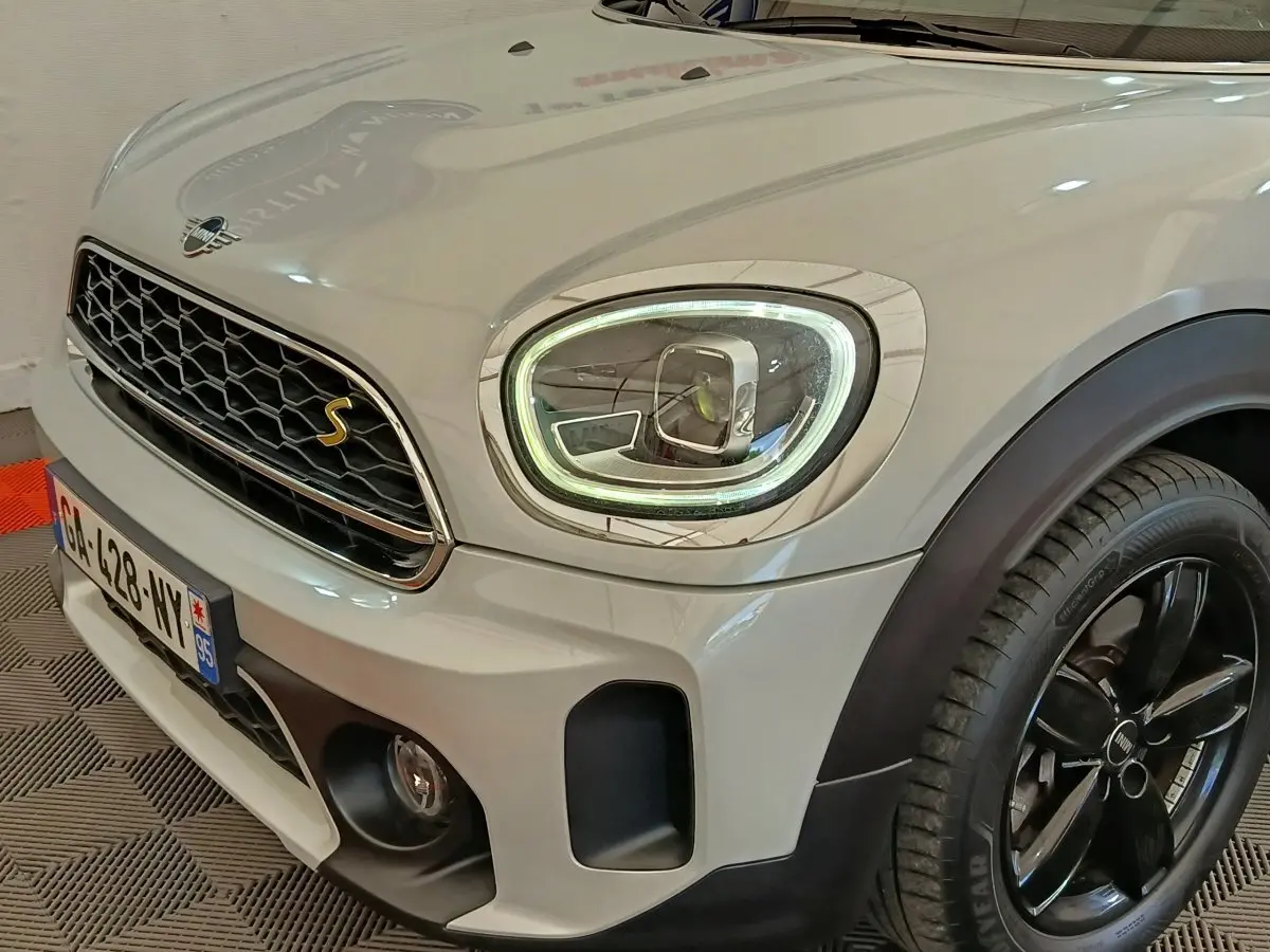 Vue 3/4 avant droit d'une MINI Countryman blanche avec phares LED allumés et jantes noires brillantes.