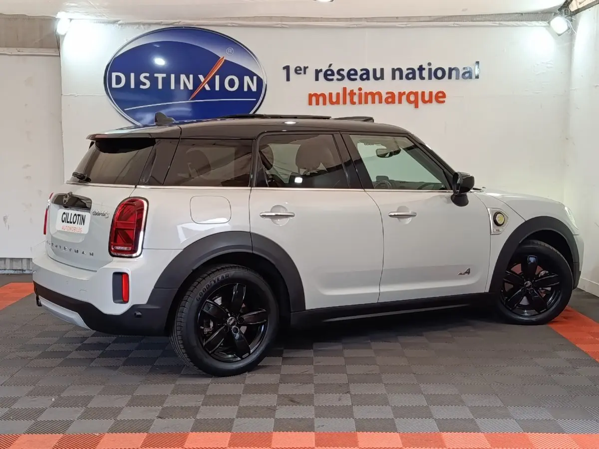 Vue côté droit d'une MINI Countryman Cooper SE hybride blanche avec toit noir et jantes noires en intérieur showroom.
