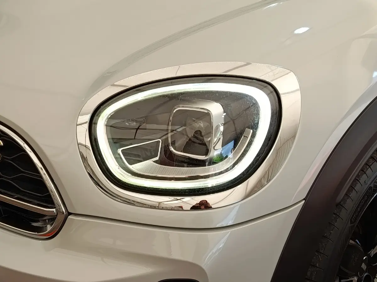 Gros plan sur le phare avant droit LED du MINI Countryman Cooper SE blanc, soulignant son contour chromé distinctif.