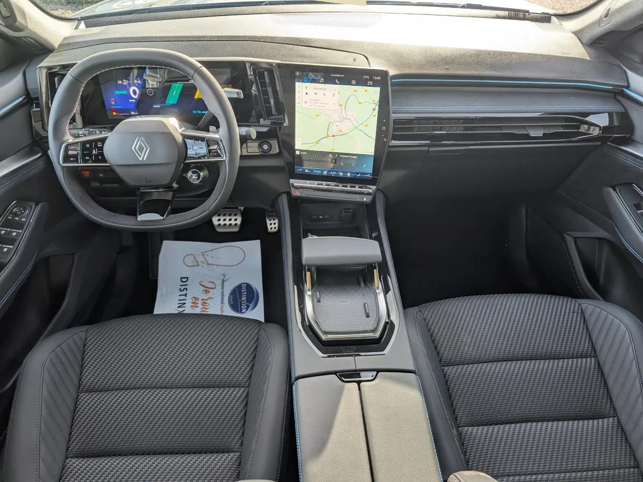 Vue intérieure avant du Renault Austral 2025 avec tableau de bord noir, écran tactile vertical et volant Alcantara.