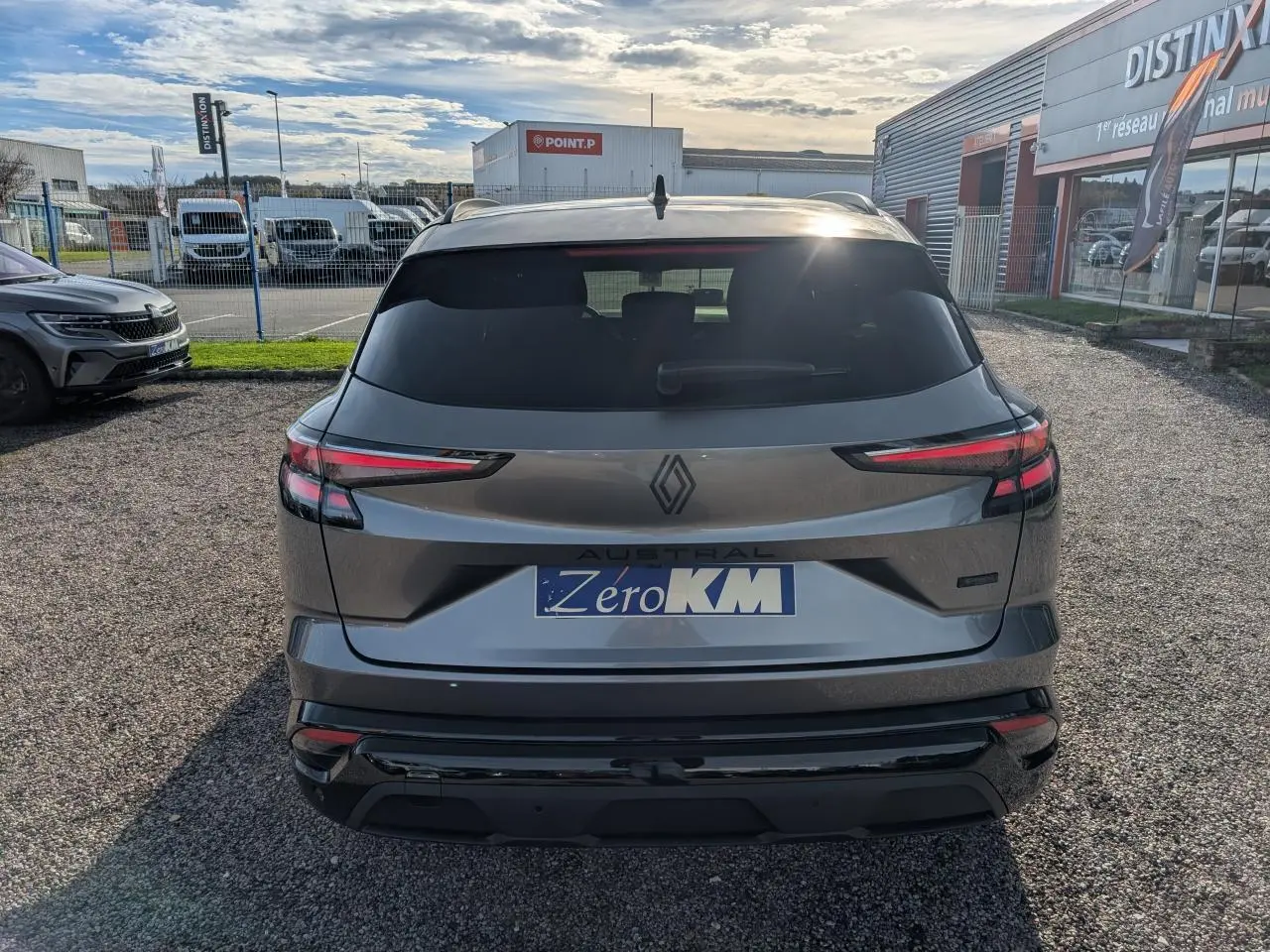 Vue arrière d'un Renault Austral gris métallisé avec toit noir étoilé et feux LED fins, stationné sur un sol gravillonné.