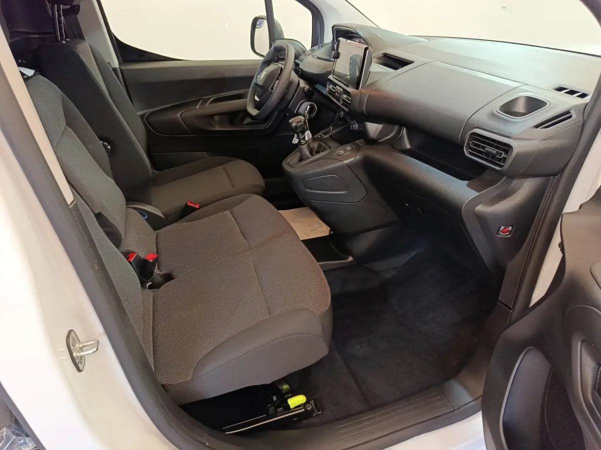 Vue intérieure côté conducteur du Peugeot Partner blanc 2025, montrant les sièges tissu gris et le tableau de bord avec écran tactile.