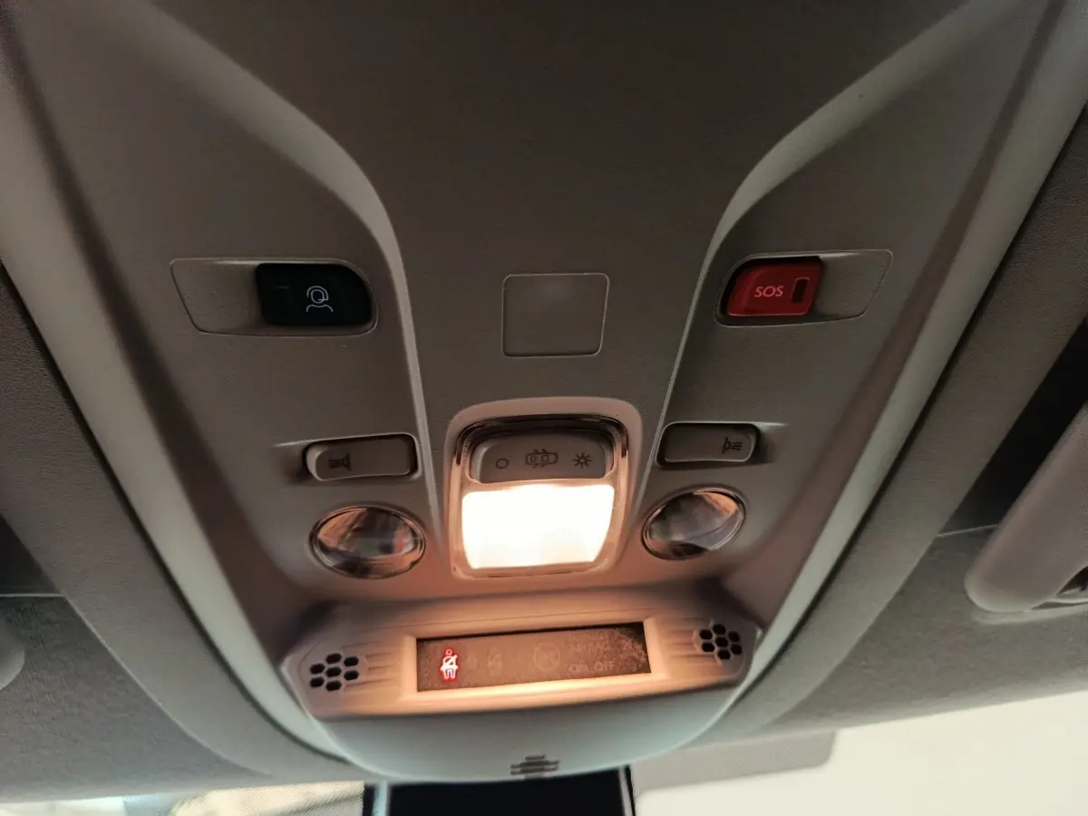 Vue en contre-plongée du plafonnier intérieur du Peugeot Partner blanc 2025 avec bouton SOS et éclairage central allumé.