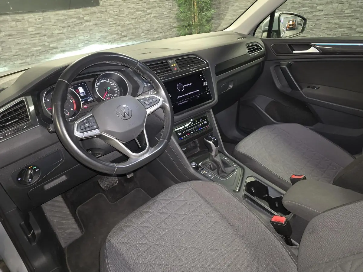 Vue intérieure avant droite du Volkswagen Tiguan 2023, sellerie tissu gris avec volant multifonctions cuir et écran tactile central.