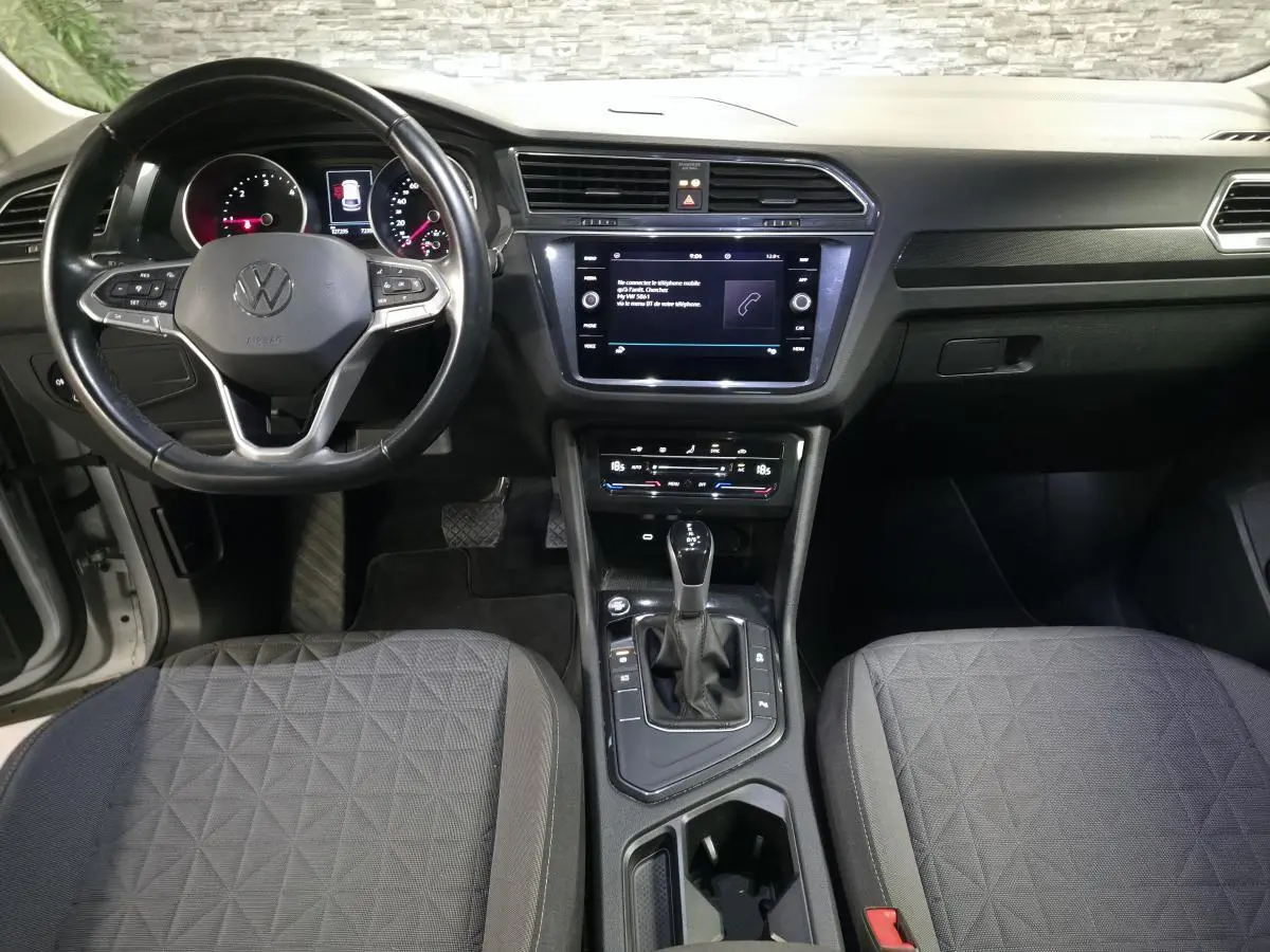 Vue intérieure avant du Volkswagen Tiguan 2023 gris, montrant volant cuir multifonctions et écran tactile central.