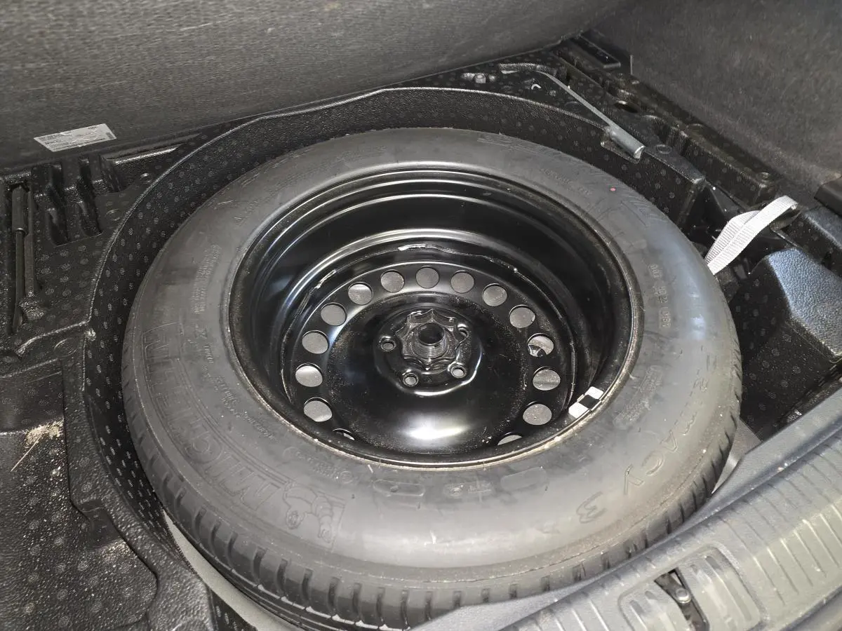 Gros plan sur la roue de secours en acier noir dans le coffre du Volkswagen Tiguan gris 2023.