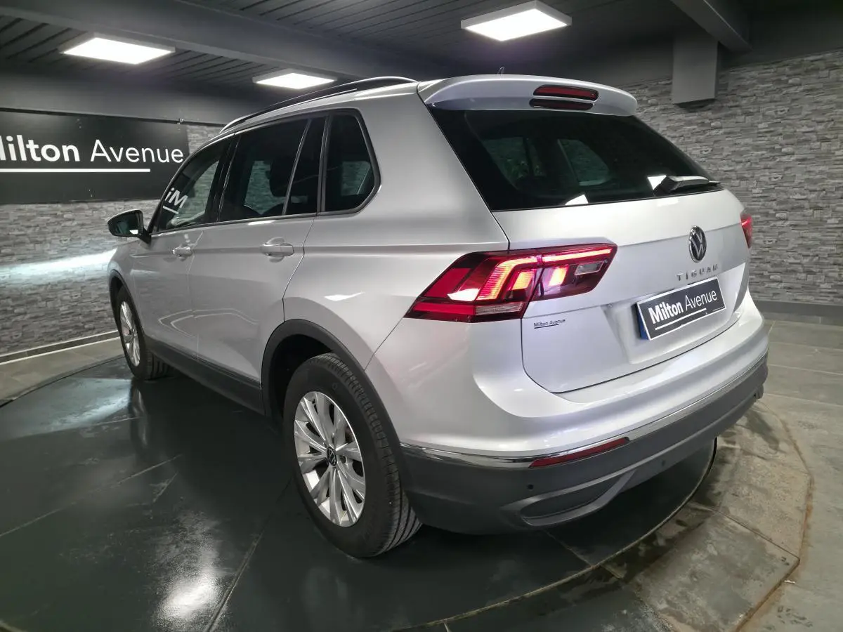Volkswagen Tiguan gris métallisé vu en 3/4 arrière droit, feux arrière LED allumés, jantes alliage 17 pouces.