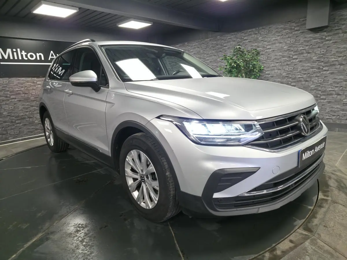 Volkswagen Tiguan gris métallisé en 3/4 avant droit avec feux LED allumés dans un showroom.
