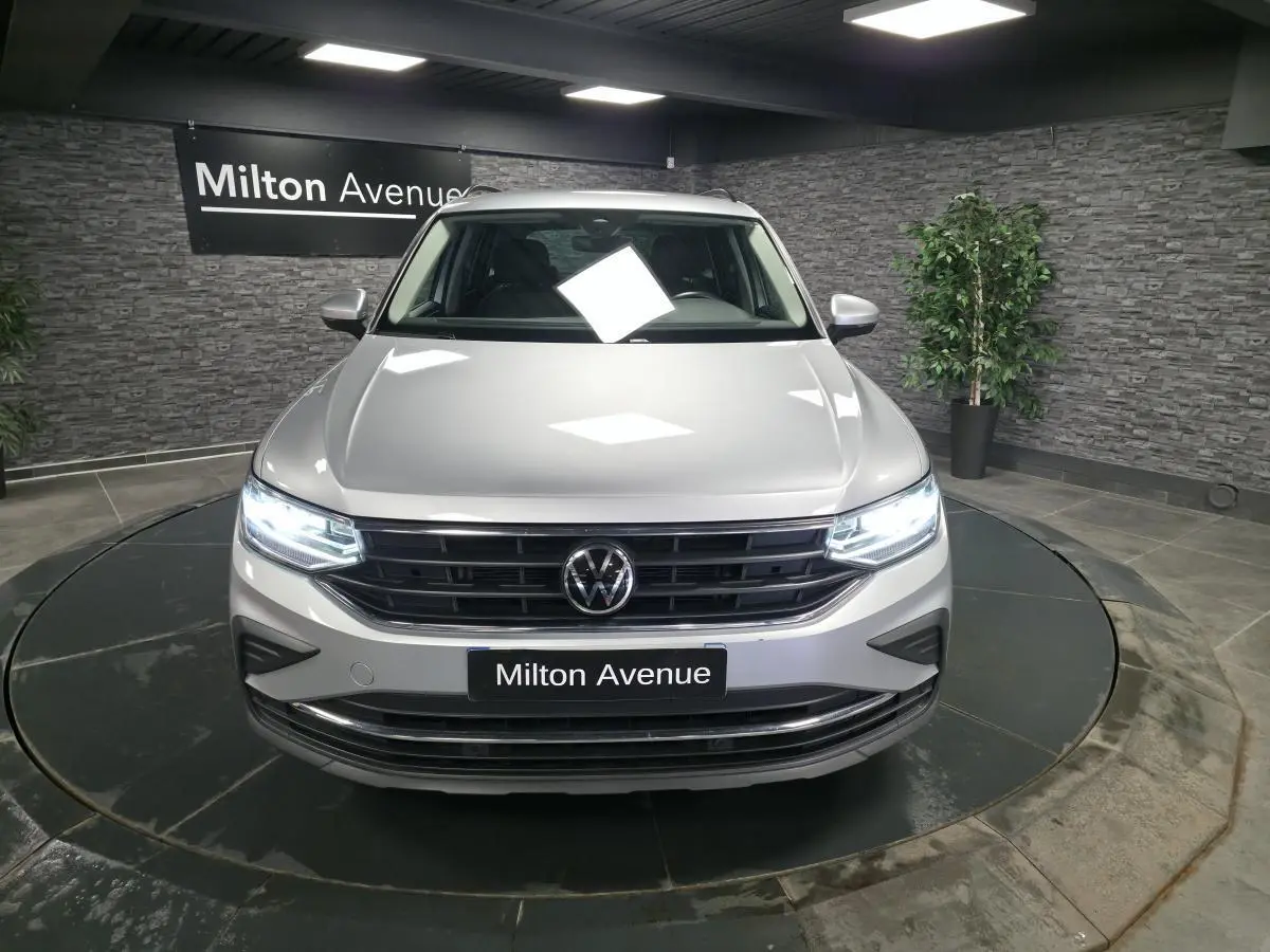 Vue avant d'un Volkswagen Tiguan gris métallisé 2023 avec phares LED allumés en showroom.