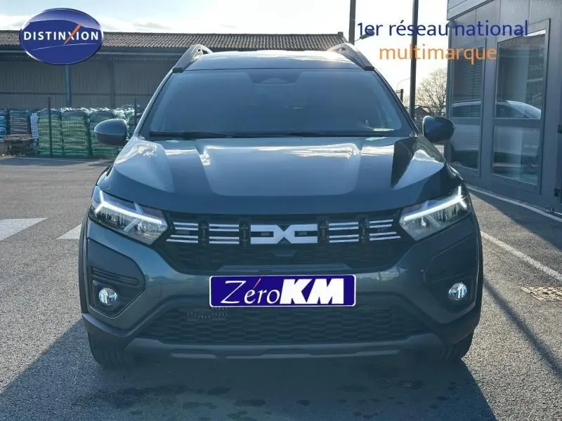 Vue de face du Dacia Jogger 2025 vert cèdre métallisé avec calandre et phares LED allumés.