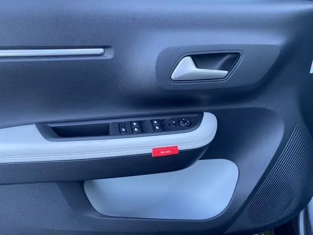 Détail de la porte intérieure côté conducteur de la Citroën C3 Hybrid 145 gris foncé avec commande des vitres et étiquette rouge "be cool".