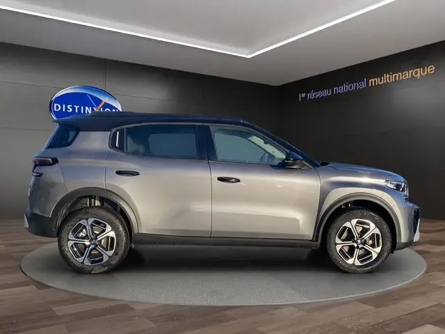 Vue de profil droit d'un Citroën C3 Hybrid 145 E-DCS6 MAX gris foncé avec jantes distinctives en exposition intérieure.