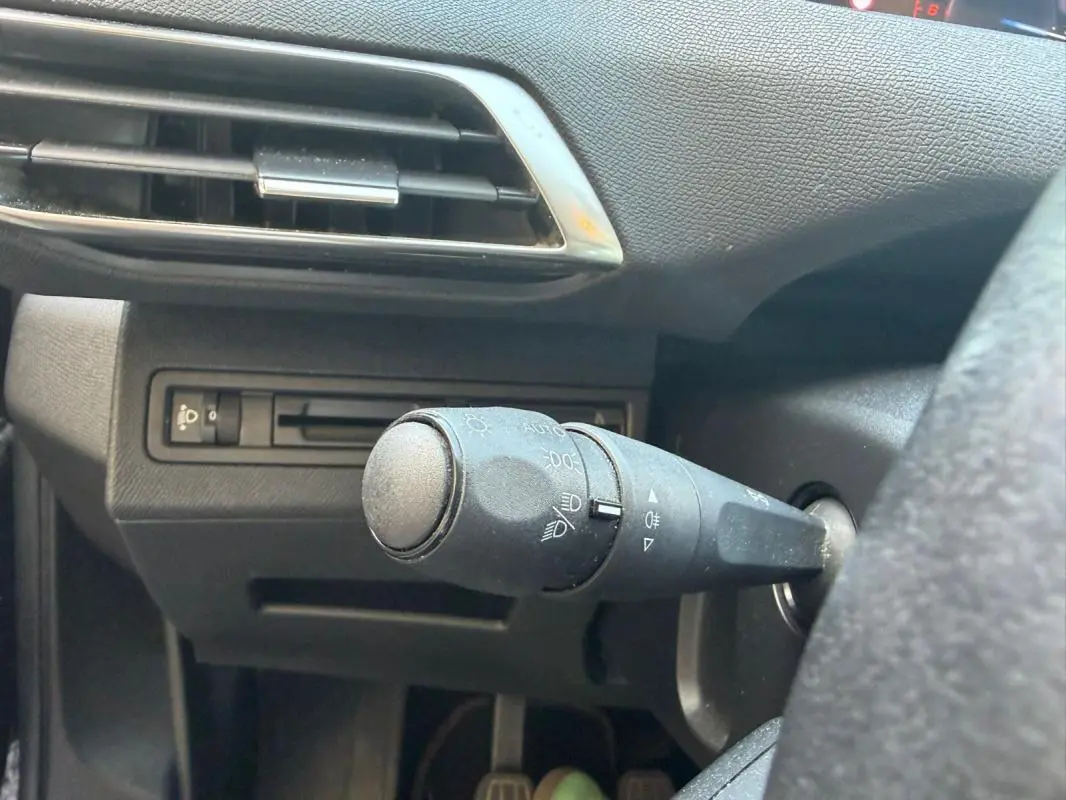Gros plan sur la commande des phares à gauche du volant dans l’habitacle noir du Peugeot 3008 2021 diesel.