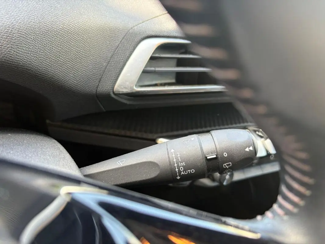 Gros plan sur la commande d’essuie-glace à gauche du volant d’un Peugeot 3008 noir, intérieur noir avec aérateur argenté.