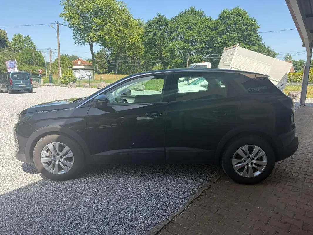 Vue de profil côté gauche d’un Peugeot 3008 noir 2021 garé sur un sol mixte gravier et pavés, avec jantes alliage.