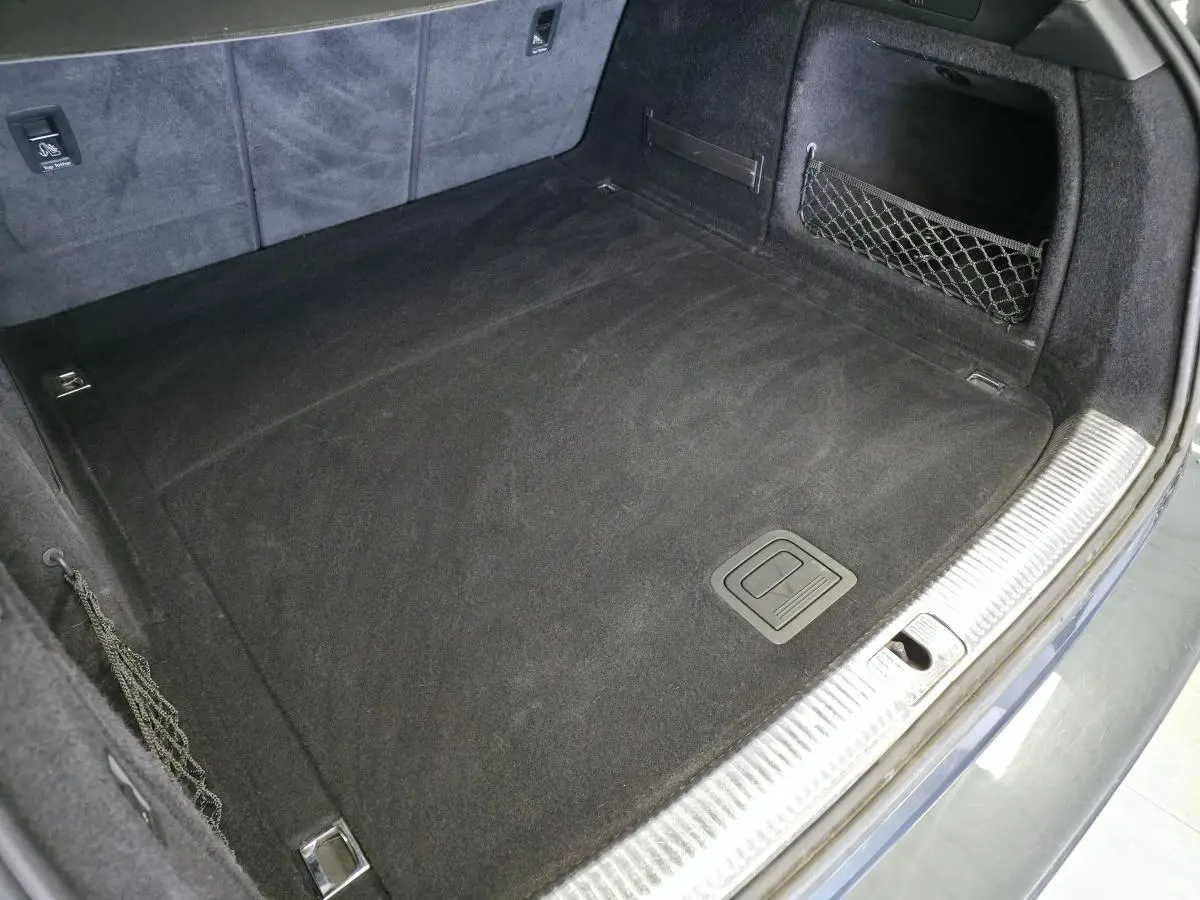 Coffre spacieux de l'Audi A4 Allroad gris, vue plongeante montrant tapis noir et filet de rangement latéral.