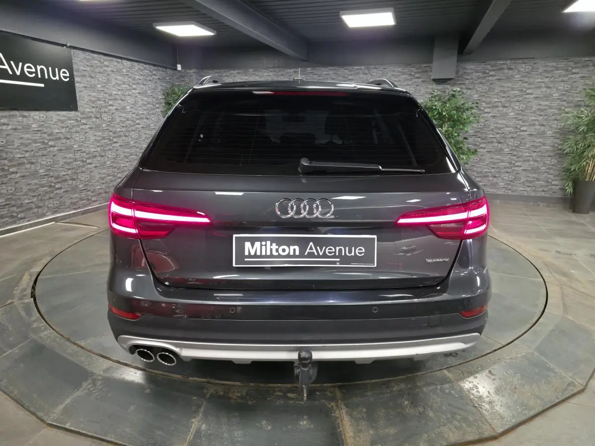 Vue arrière d'une Audi A4 Allroad Quattro gris métallisé avec feux allumés et crochet d'attelage visible.