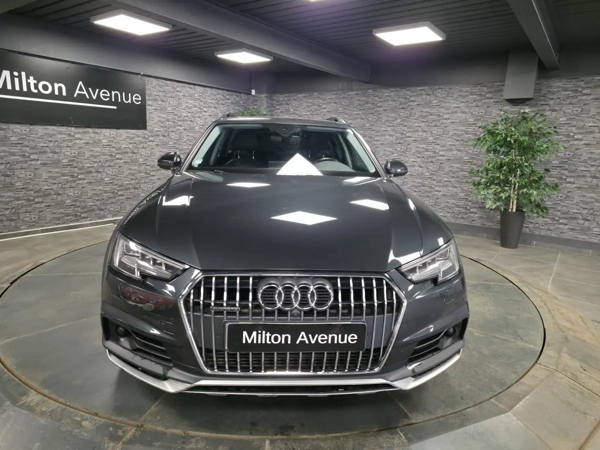 Audi A4 Allroad Quattro gris vue de face dans un showroom avec éclairage et décor mural en pierre grise.