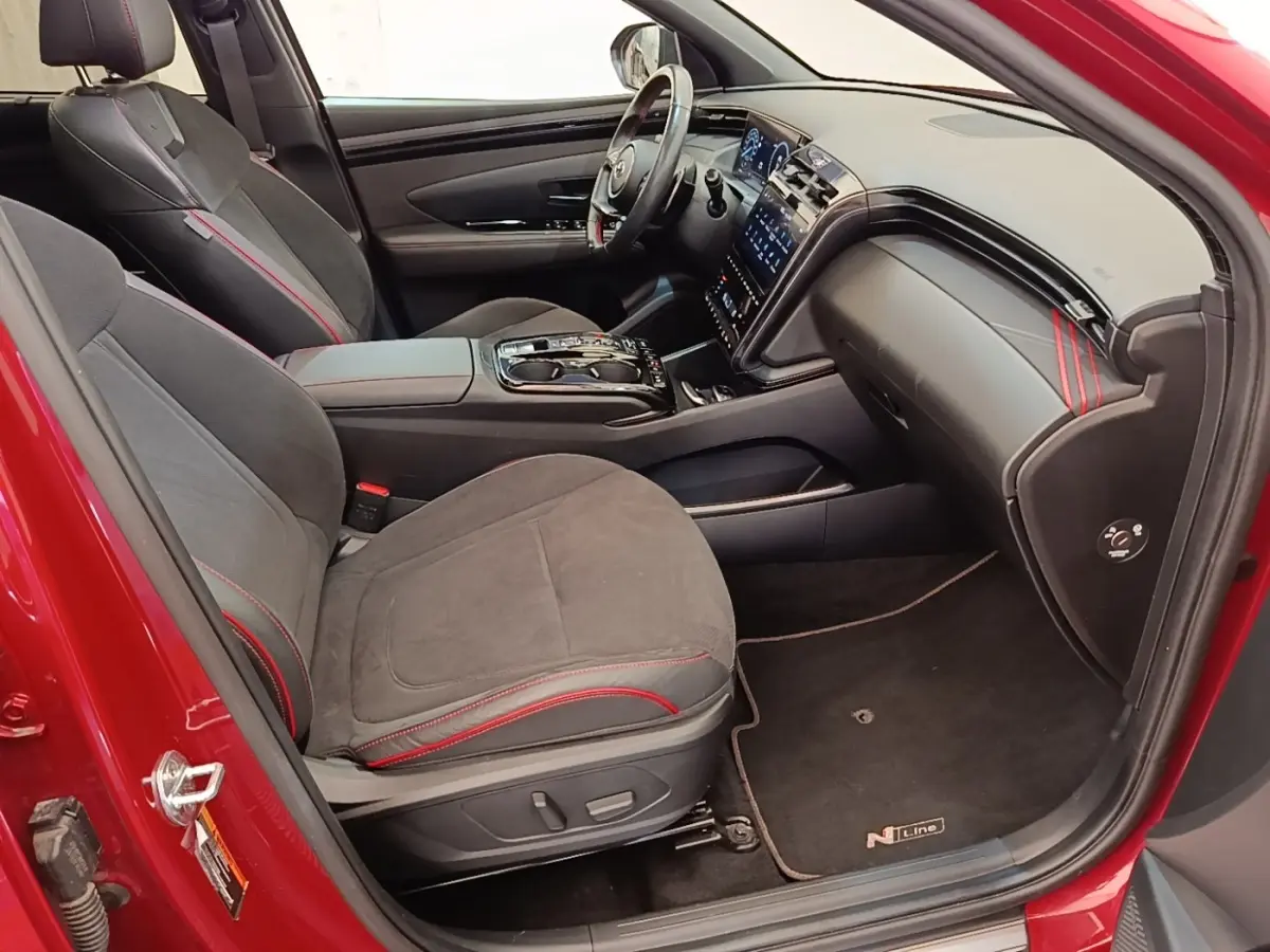 Vue intérieure côté conducteur du Hyundai Tucson rouge 2022, sièges noirs avec surpiqûres rouges et tableau de bord moderne.