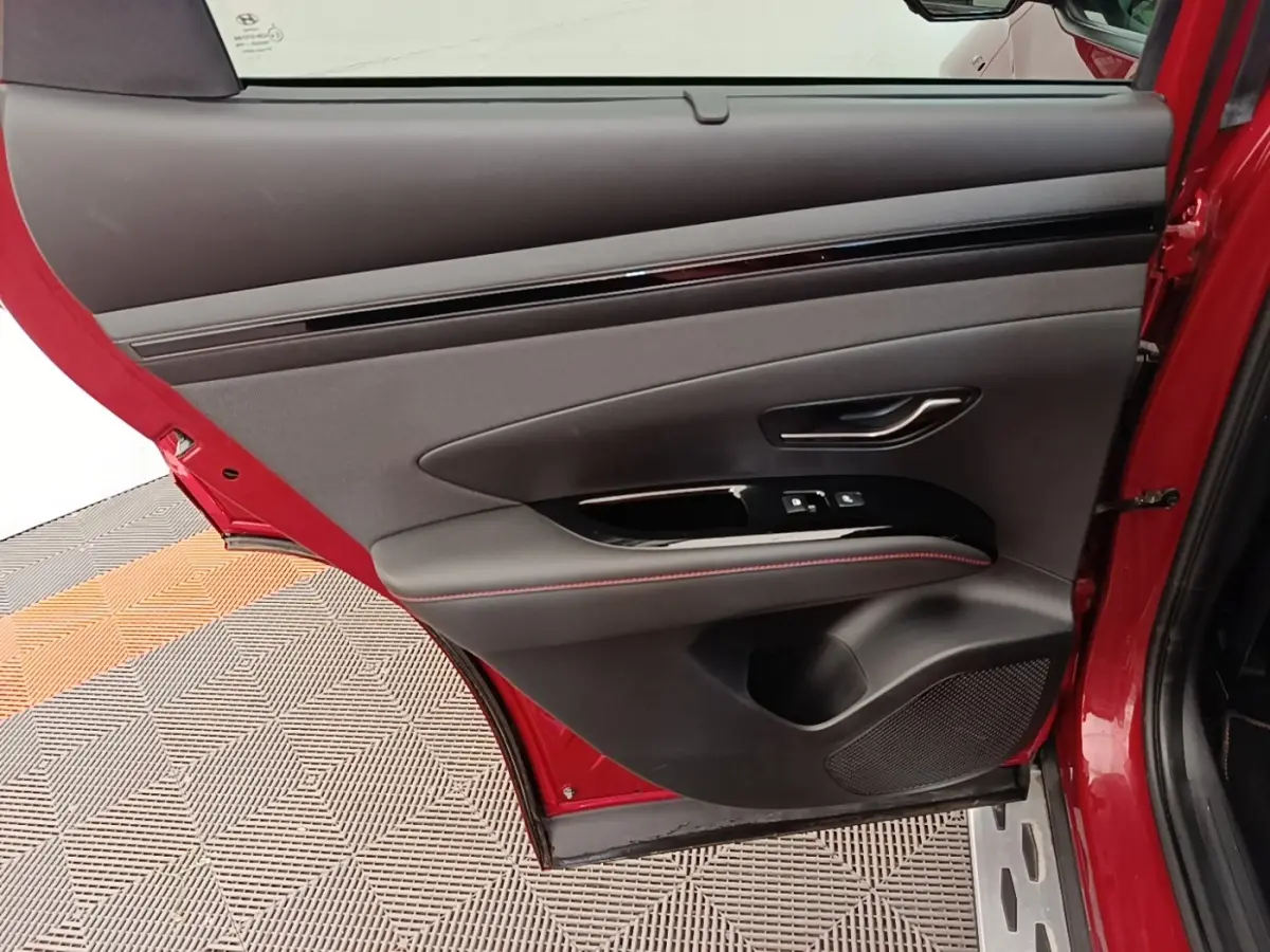 Vue rapprochée de la porte arrière gauche rouge du Hyundai Tucson 2022 avec garniture noire et surpiqûres rouges.