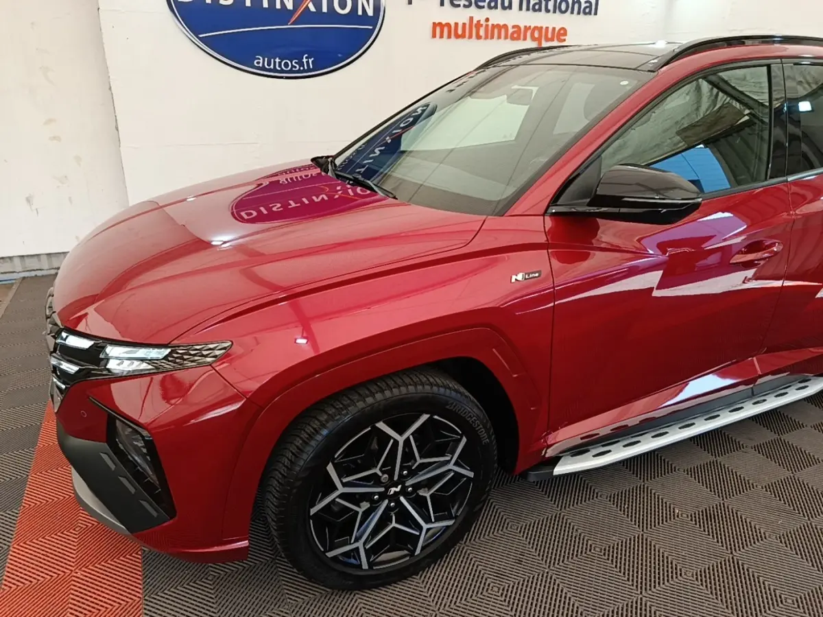 Vue 3/4 avant droit d'un Hyundai Tucson rouge N Line avec jantes noires et marchepieds argentés.